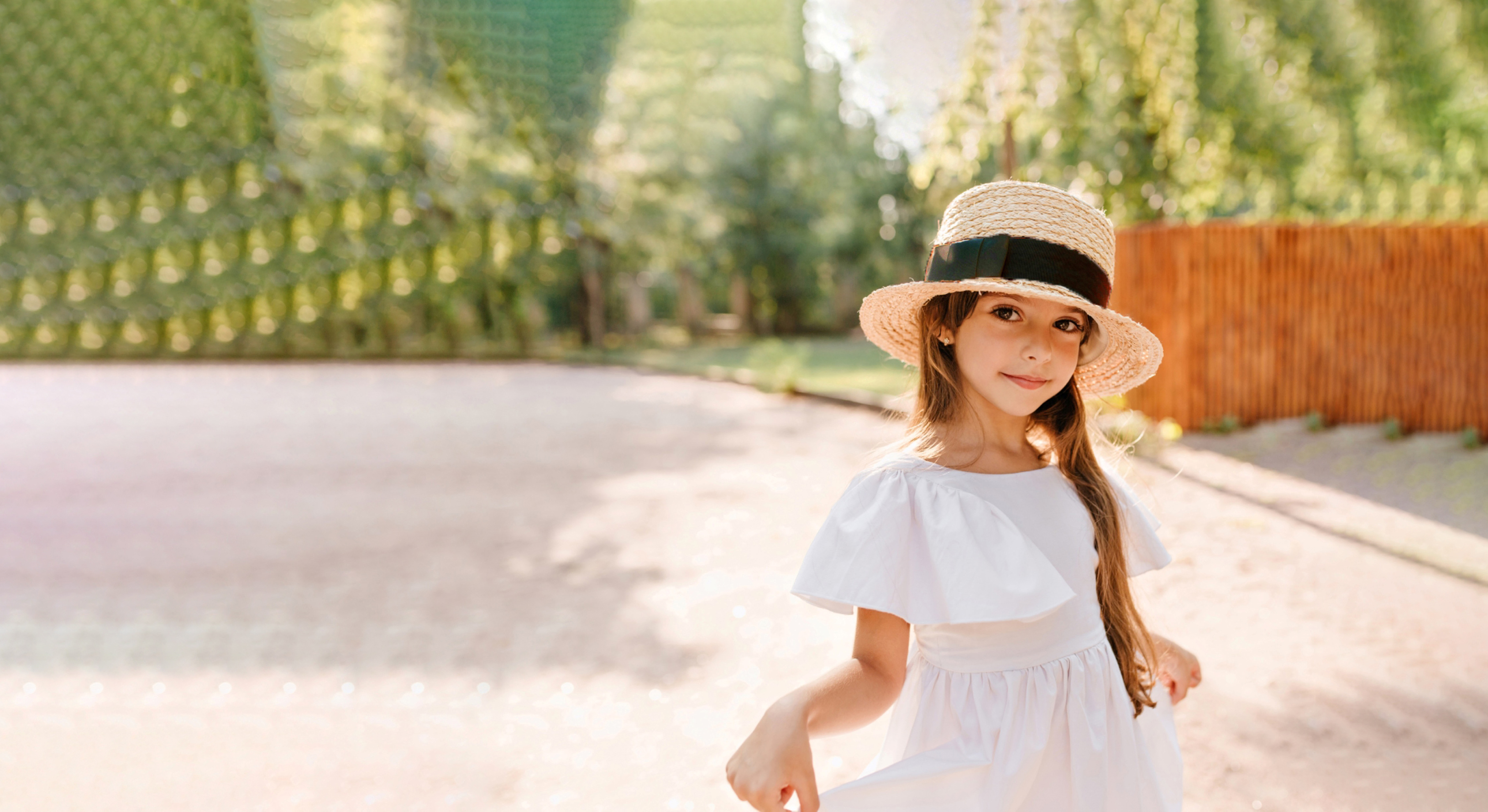 pretty-girl-big-straw-hat-playing-with-her-white-dress-while-posing-park-with-wooden-fence-portrait-lovely-female-kid-wears-boater-decorated-with-ribbon-dancing-road